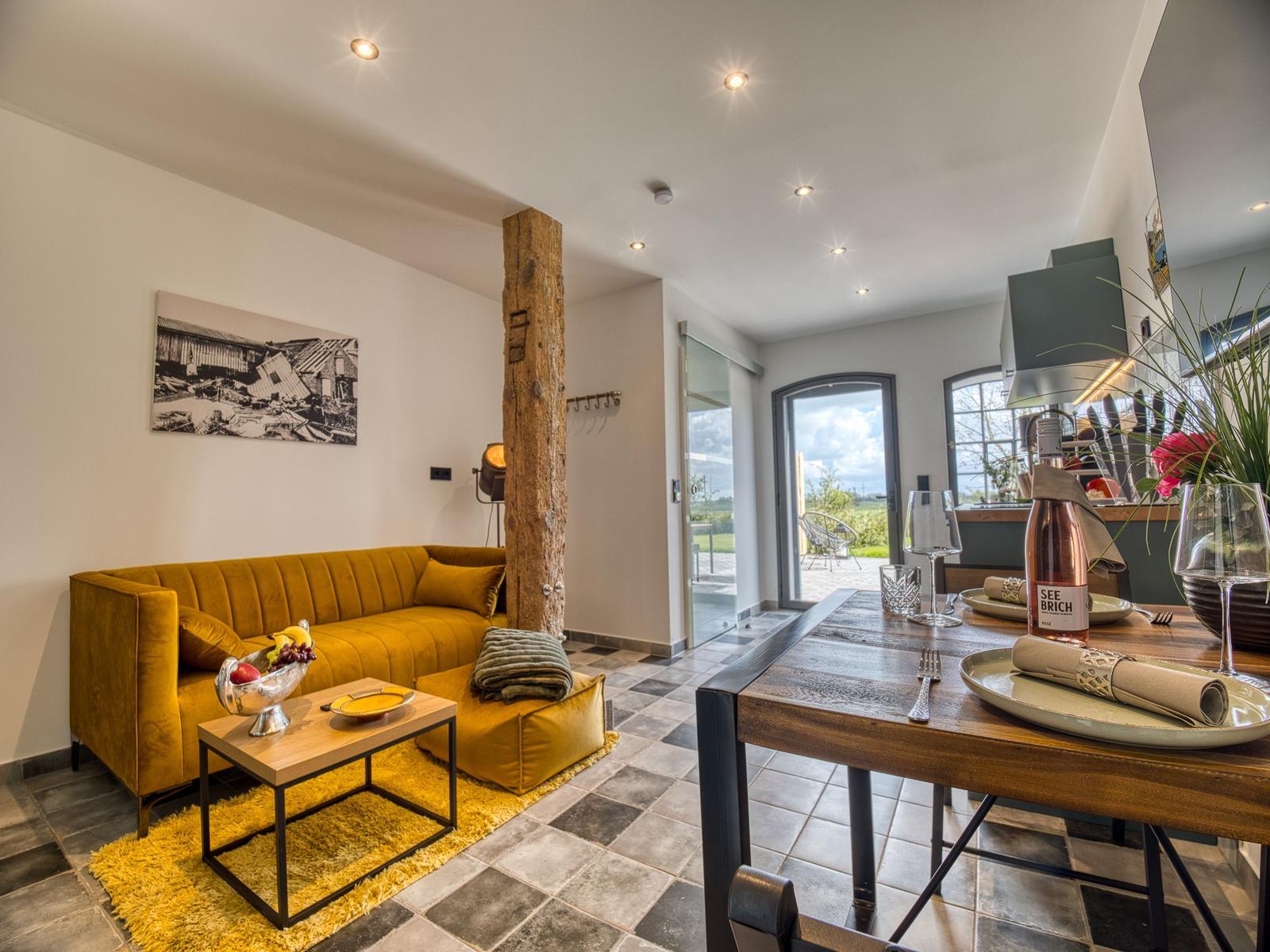 Wohn- und Essbereich mit gelbem Sofa, Holztisch und rustikaler Säule.