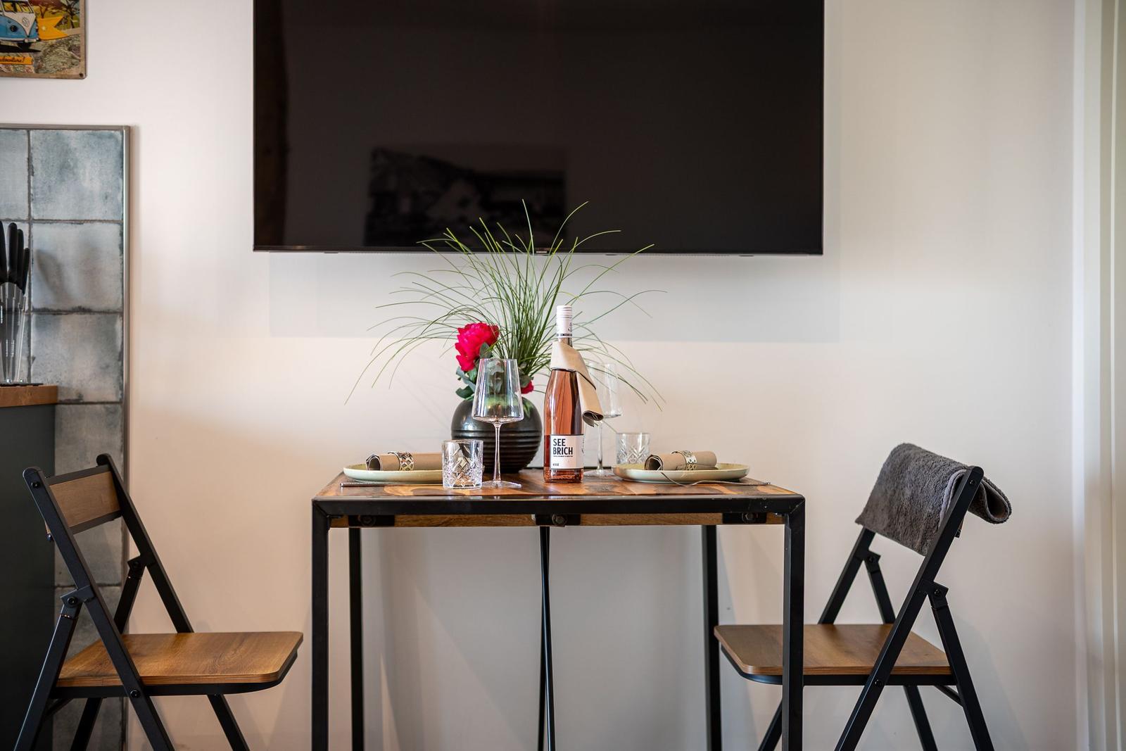 Esstisch mit zwei Stühlen, Fernseher und Blumendekoration.