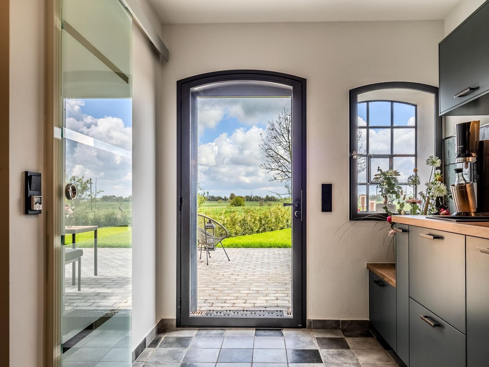 Eingangsbereich mit Blick auf Terrasse und Feld. Küche mit Arbeitsplatte und Fenster.