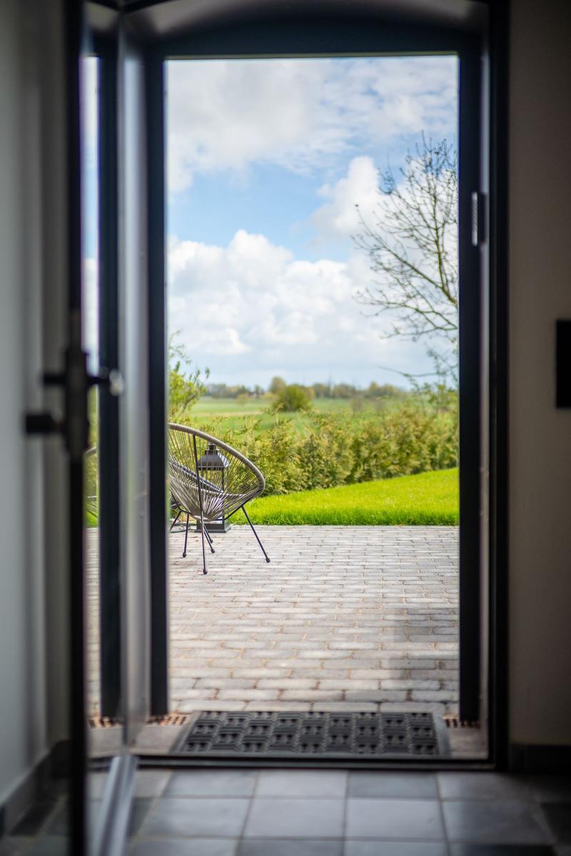Durch die Tür blickt man auf eine Terrasse mit Stuhl und grüne Landschaft.