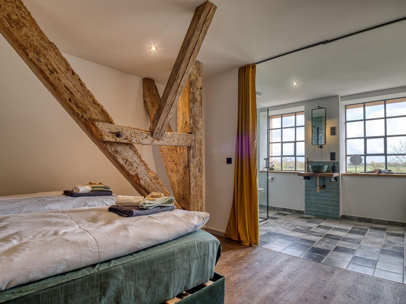 Schlafzimmer mit massivem Holzgestell und angrenzender Dusche mit Fenster.