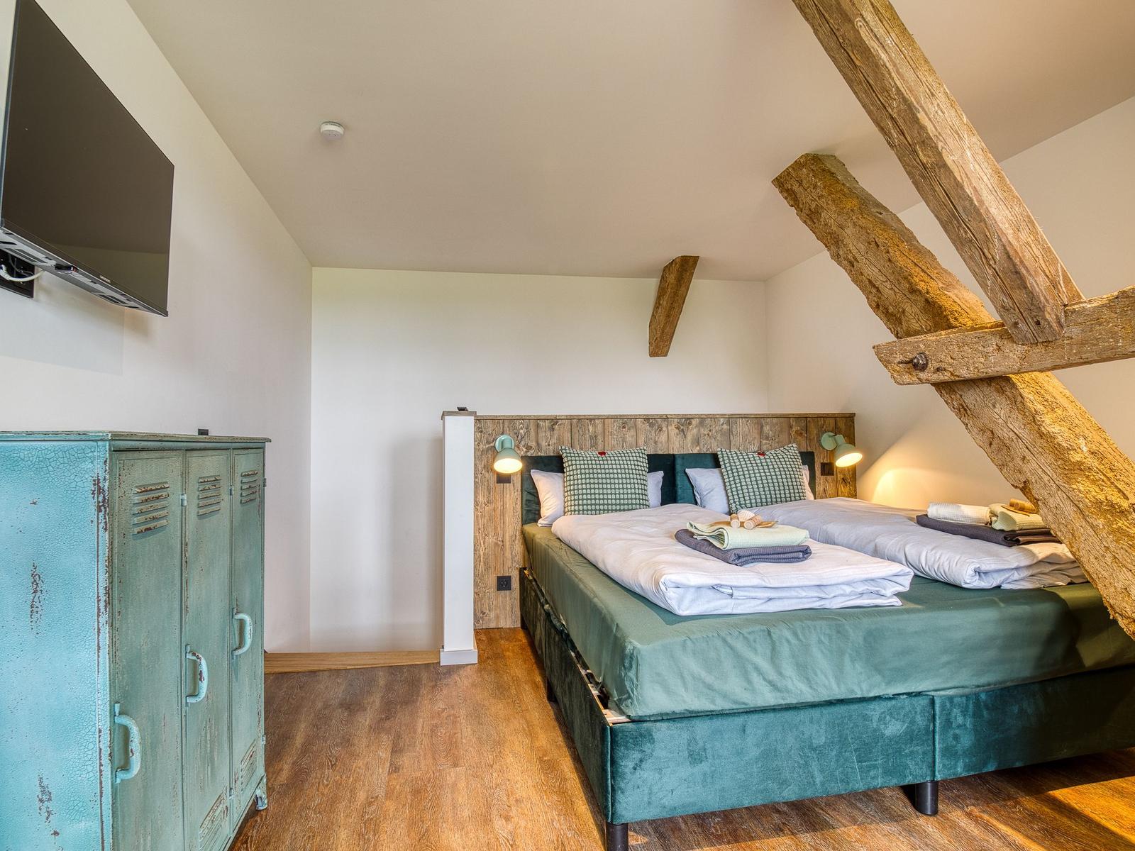 Schlafzimmer mit Doppelbett, Holzbalken und Fernseher an der Wand.