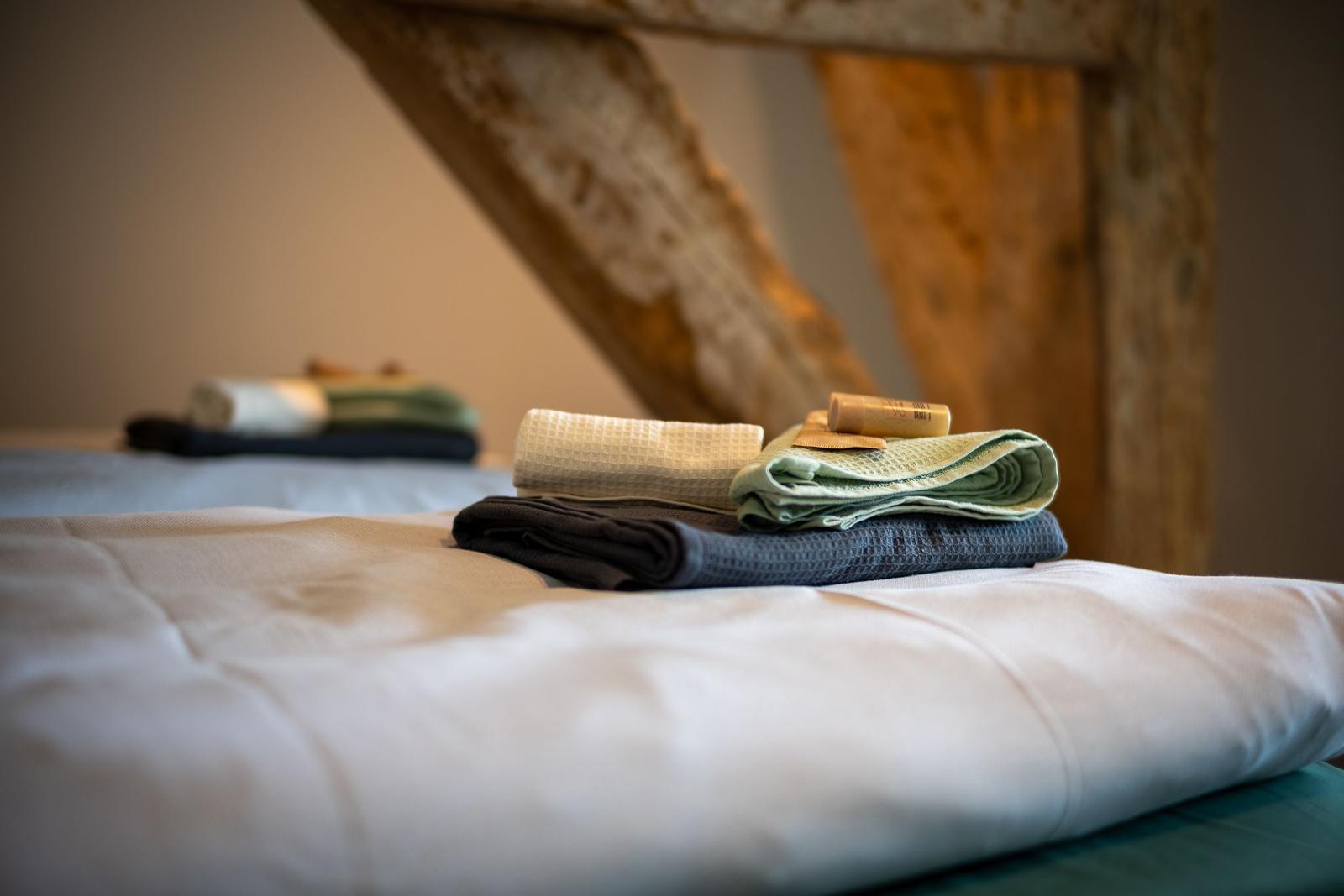 Faltbare Handtücher liegen auf einem Bett mit weißer Bettwäsche.