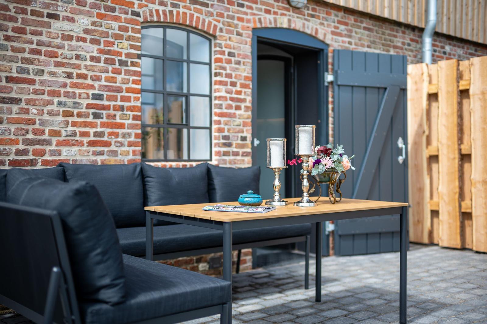 Außenbereich mit Sofa, Tisch und Blumen vor Backsteinmauer