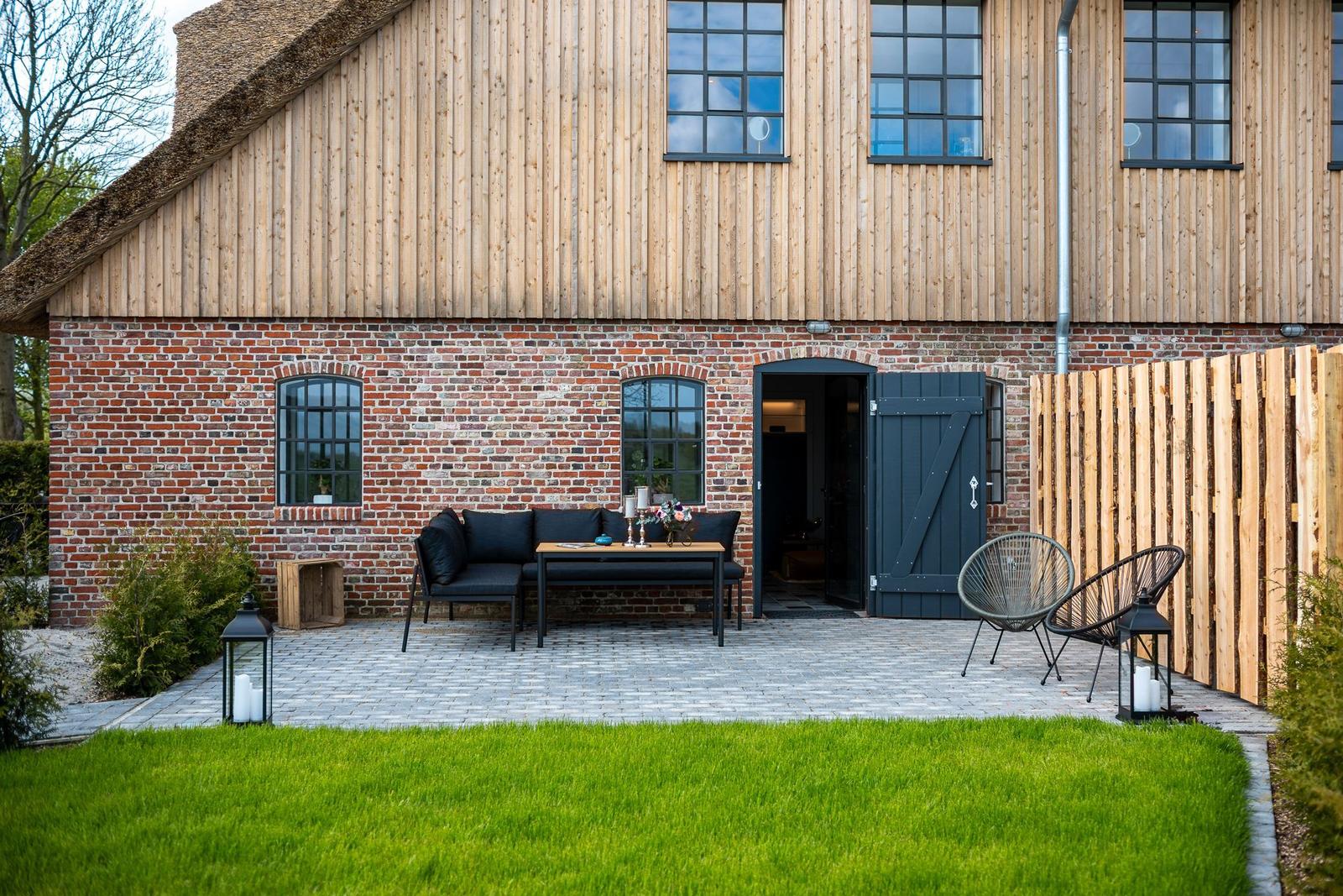 Haus mit Holz- und Ziegelwand, Terrasse mit Sitzgelegenheiten und Garten.