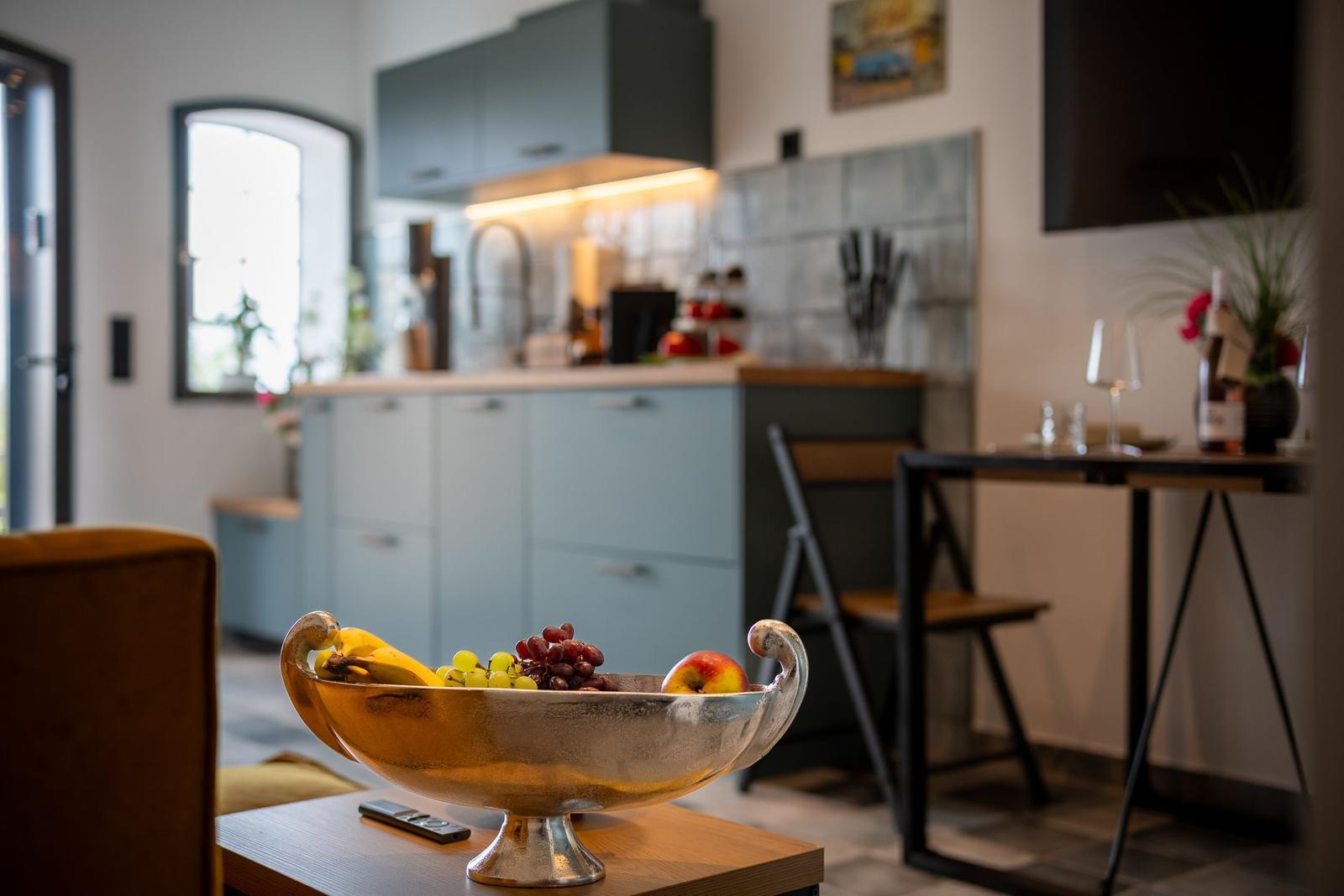 Küche mit Obstschale und Essbereich im Hintergrund.