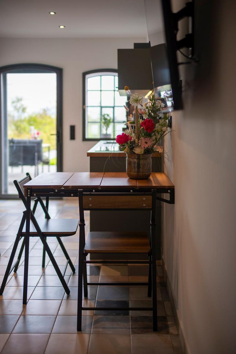 Esstisch mit Stühlen und Blumenarrangement vor Küchenbereich.