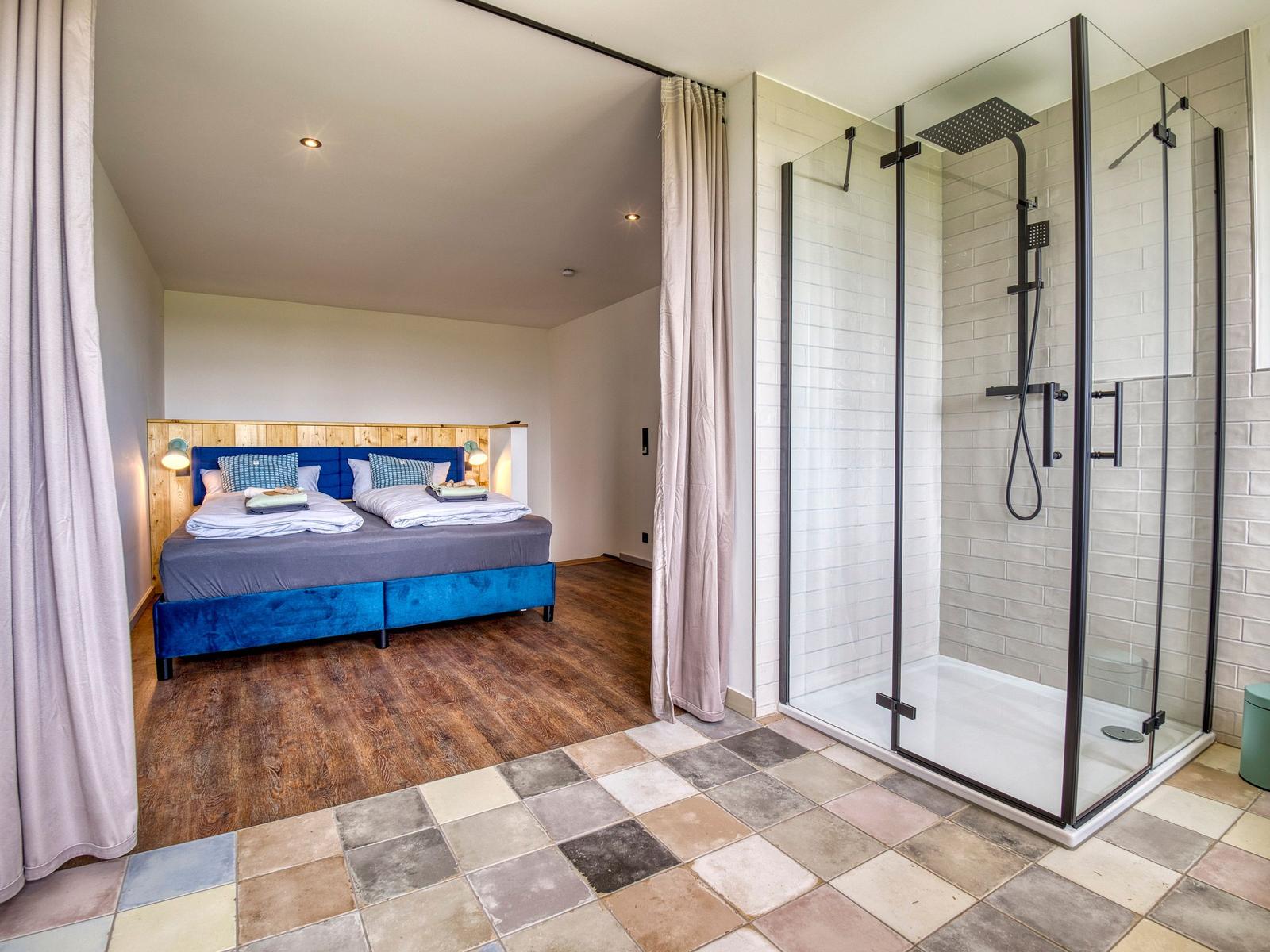 Schlafzimmer mit Doppelbett und angrenzender Dusche mit Glasabtrennung.
