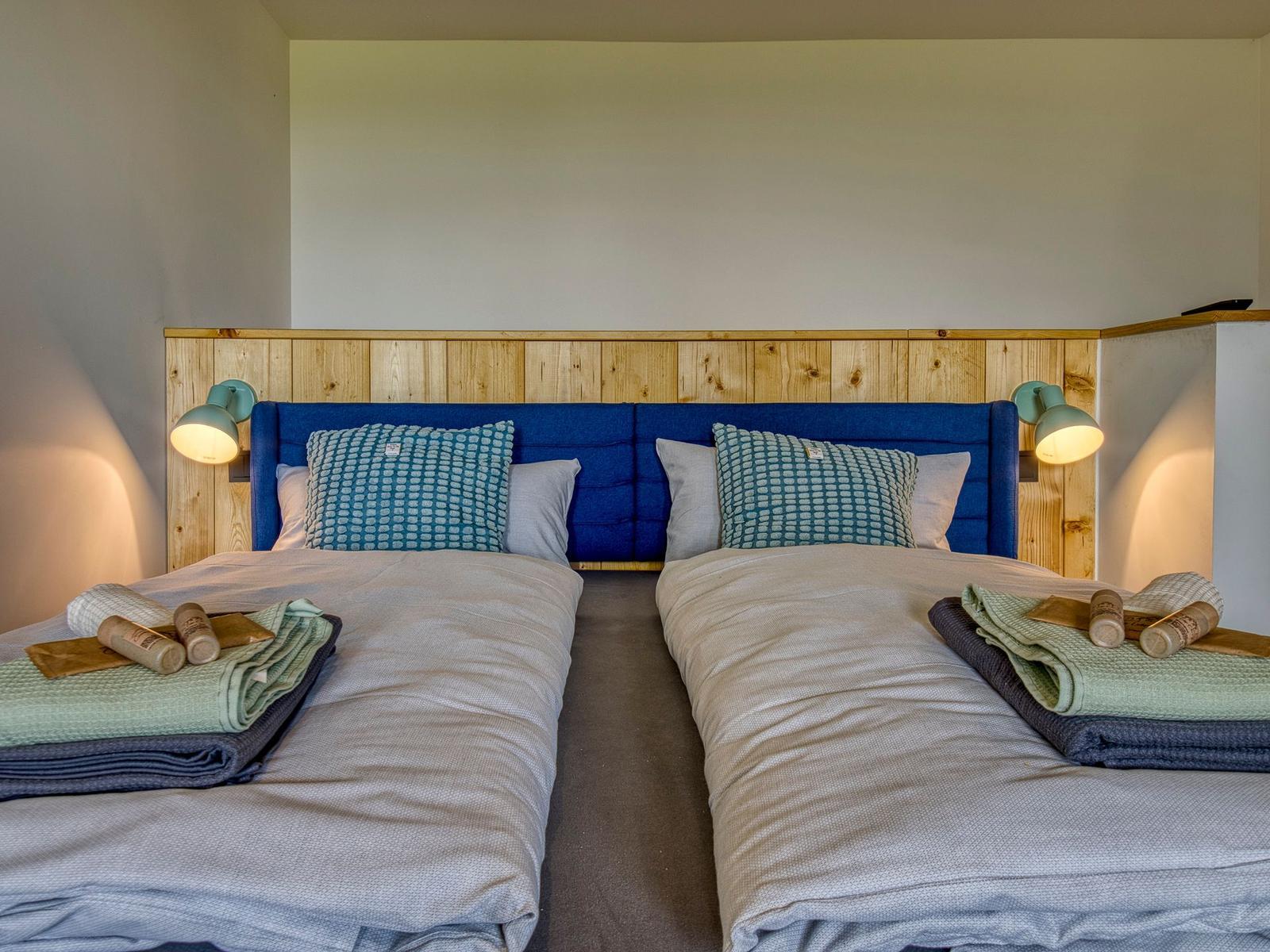 Zwei Betten mit blauem Kopfteil und Holzpaneelen an der Wand.
