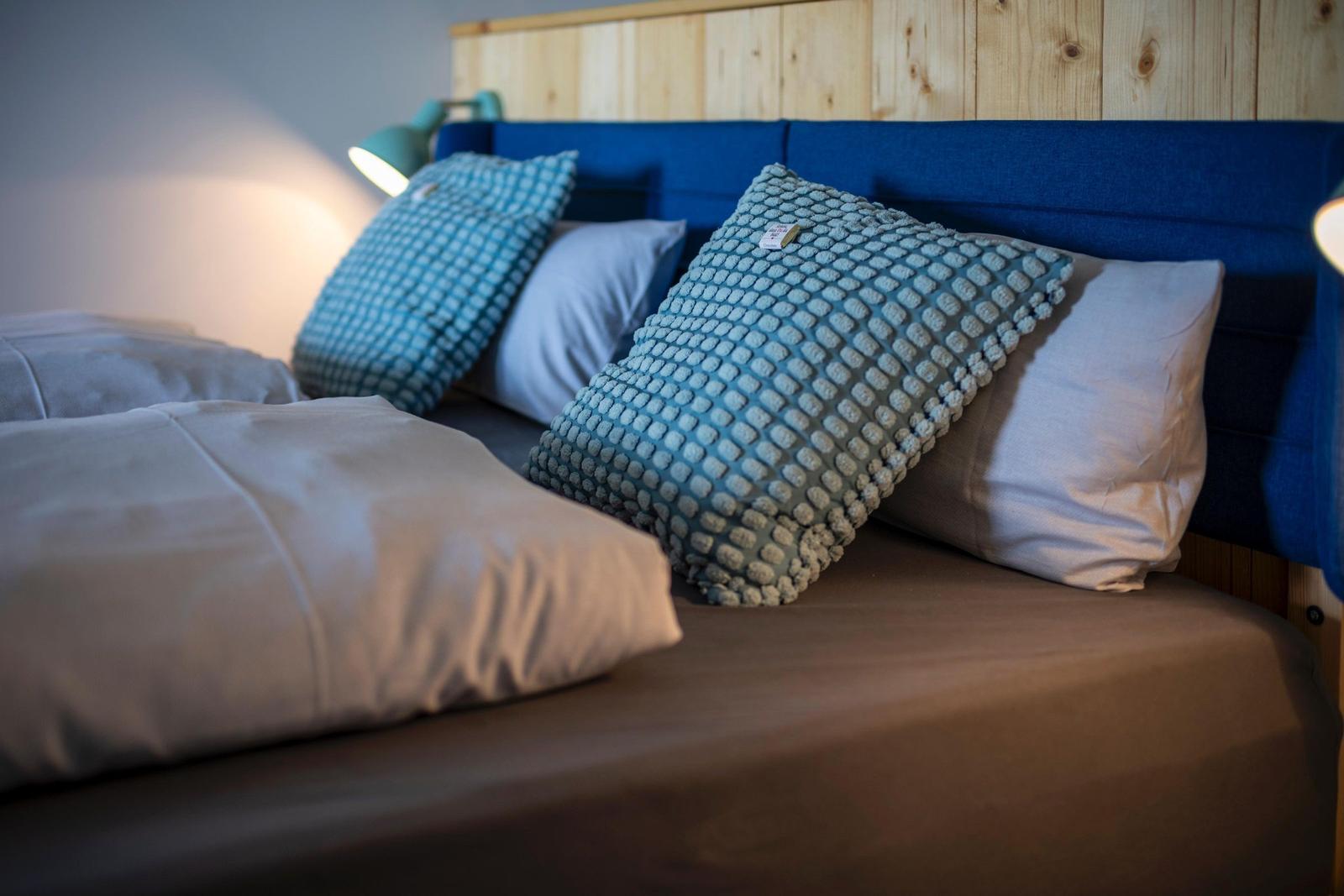 Bettkopfteil mit blauem Polster und Holzverkleidung, dekoriert mit Kissen und Bettwäsche.