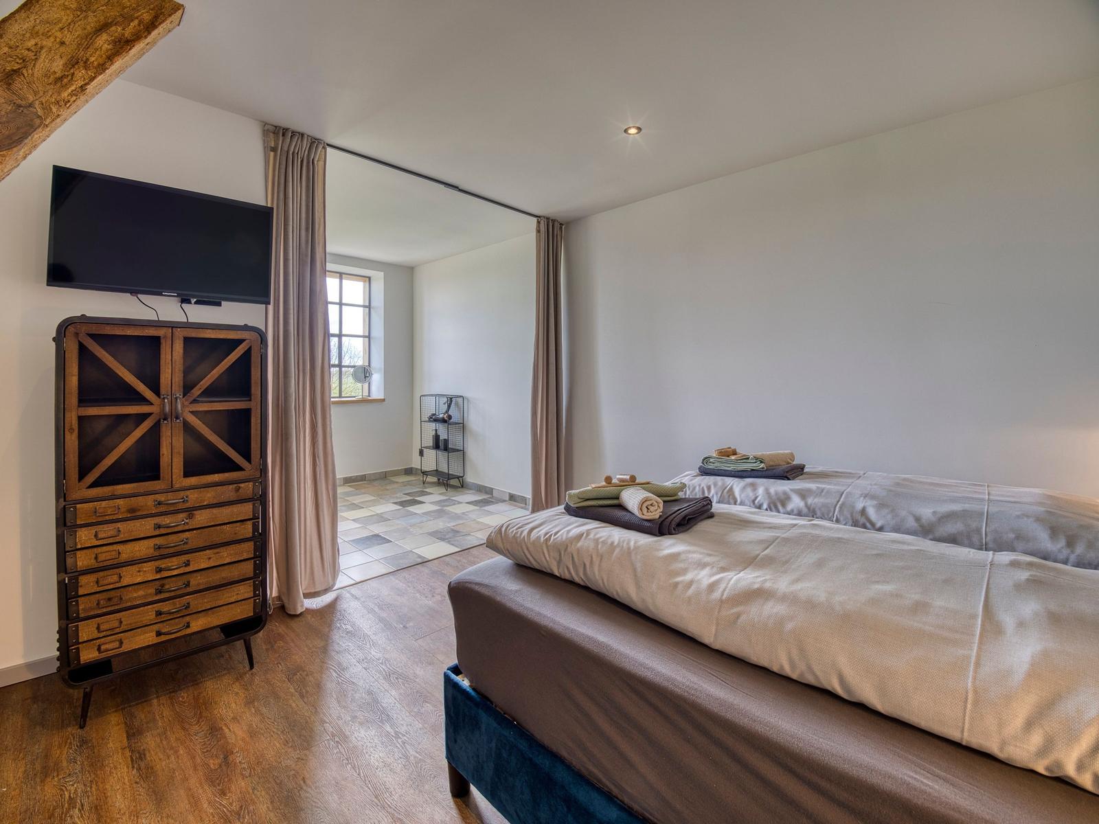 Schlafzimmer mit Doppelbett, Fernseher und Blick in angrenzenden Raum.