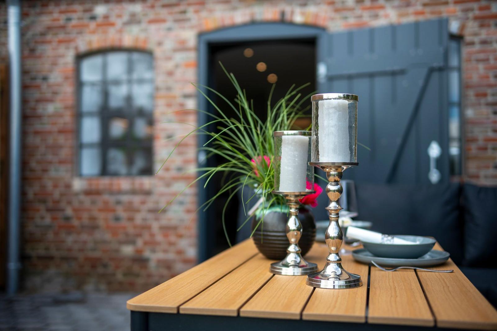 Außenbereich mit Holztisch, Kerzenhaltern und Pflanze vor Backsteinmauer