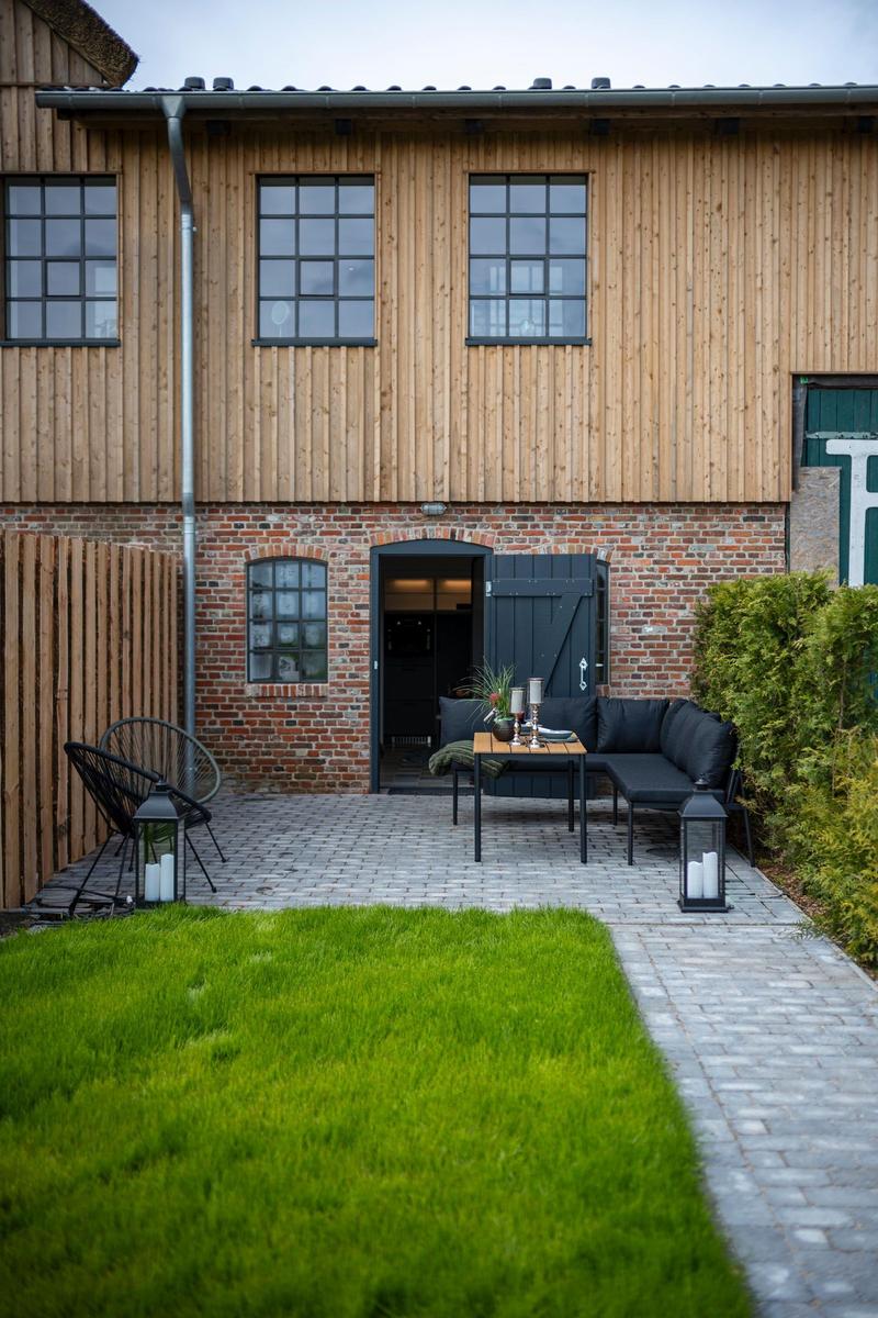 Hinterhof mit Sitzbereich, Grasfläche und Steinplattenweg vor Holz- und Ziegelhaus.