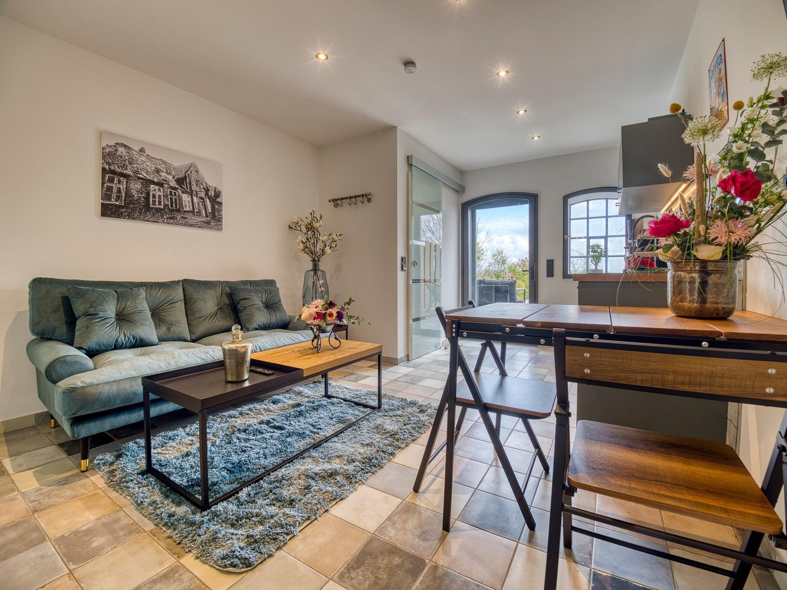Wohn- und Essbereich mit Sofa, Tisch und Stühlen. Fenster und Tür zur Aussicht.
