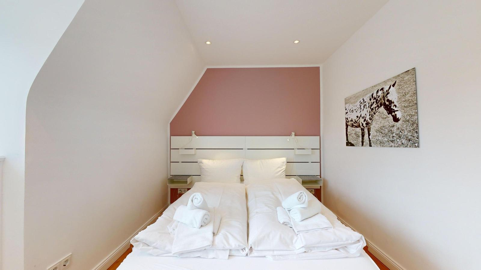Schlafzimmer mit Doppelbett, rosa Wand und Pferd-Bild an der Wand.