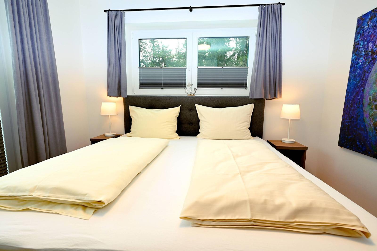 Schlafzimmer mit Doppelbett, zwei Nachttischen und Fenster mit Jalousien.