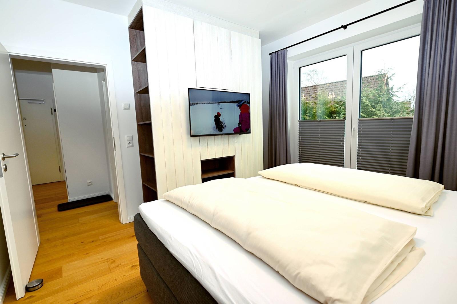 Schlafzimmer mit Bett, Fernseher und Fenster mit Blick nach außen.