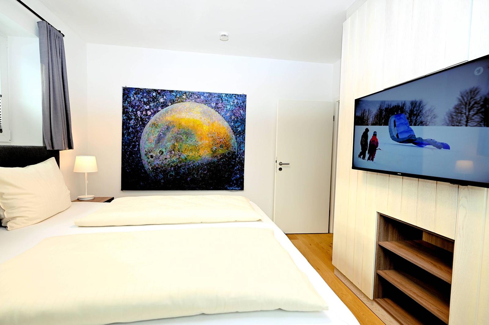 Schlafzimmer mit Bett, Wandbild und Fernseher an Wand.