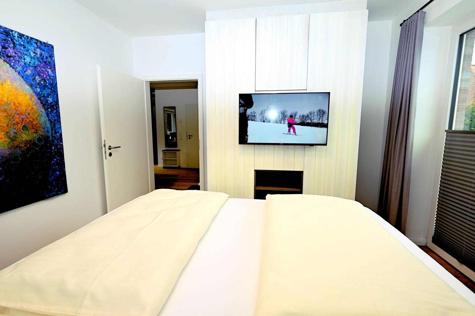 Schlafzimmer mit Bett, Fernseher und Wandbild.