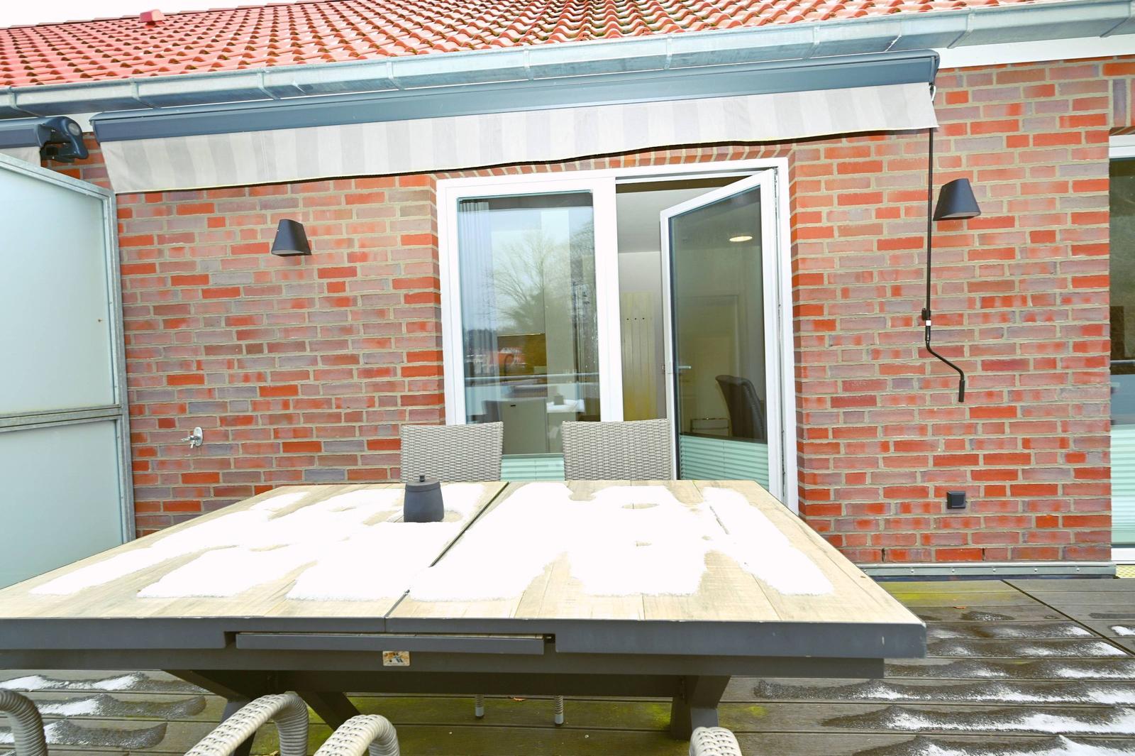 Terrasse mit Tisch und Stühlen vor rotem Ziegelhaus mit Schiebetür.