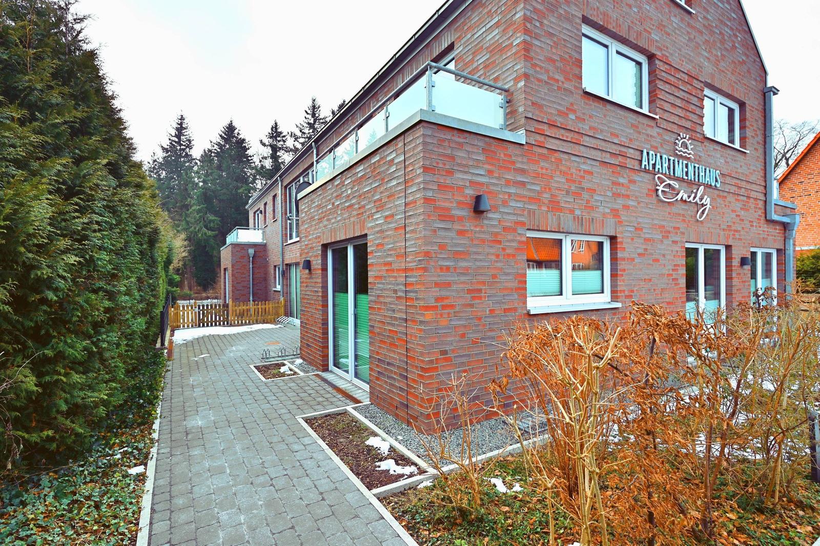 Apartmenthaus Emily mit Balkon, Holztor und gepflastertem Weg.
