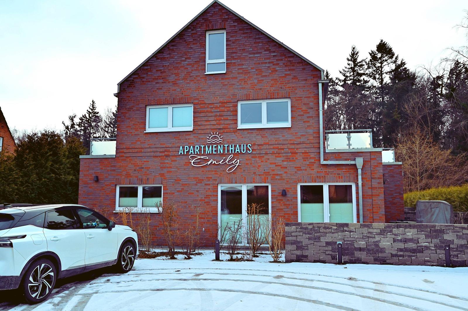 Rotes Backsteinhaus mit Schriftzug. Schnee bedeckt den Boden. Ein Auto parkt vorne.