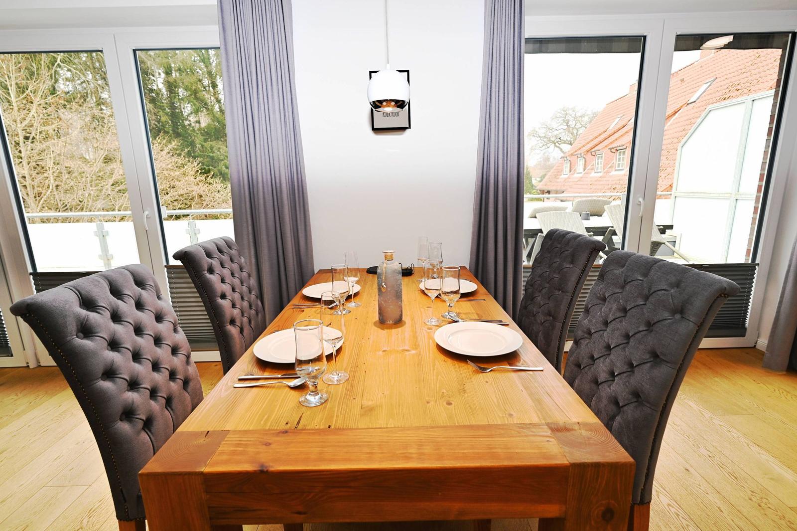 Esszimmer mit Holztisch und gepolsterten Stühlen. Durchgänge zu Balkon und Garten.