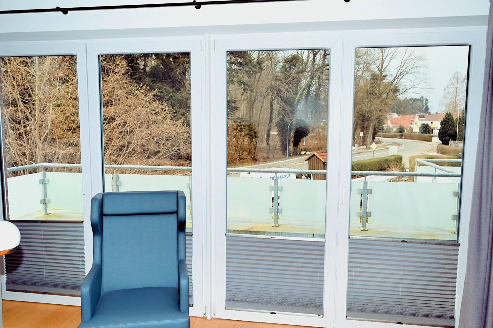 Ein blauer Sessel vor großen Fenstern mit Blick auf Balkon und Straße.