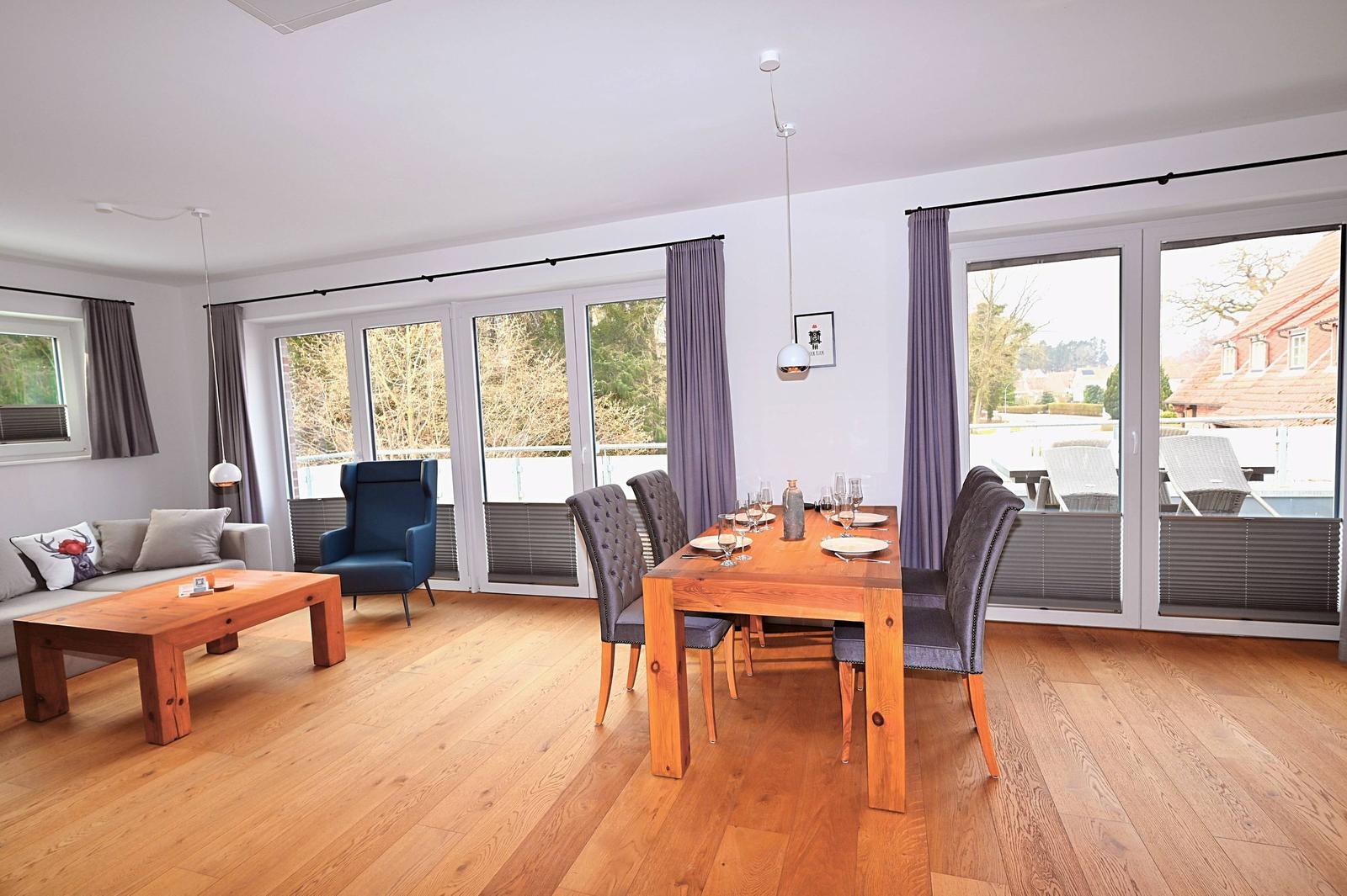 Wohn- und Essbereich mit Holzboden, Tisch und Stühlen, Sofa und Blick auf Balkon.