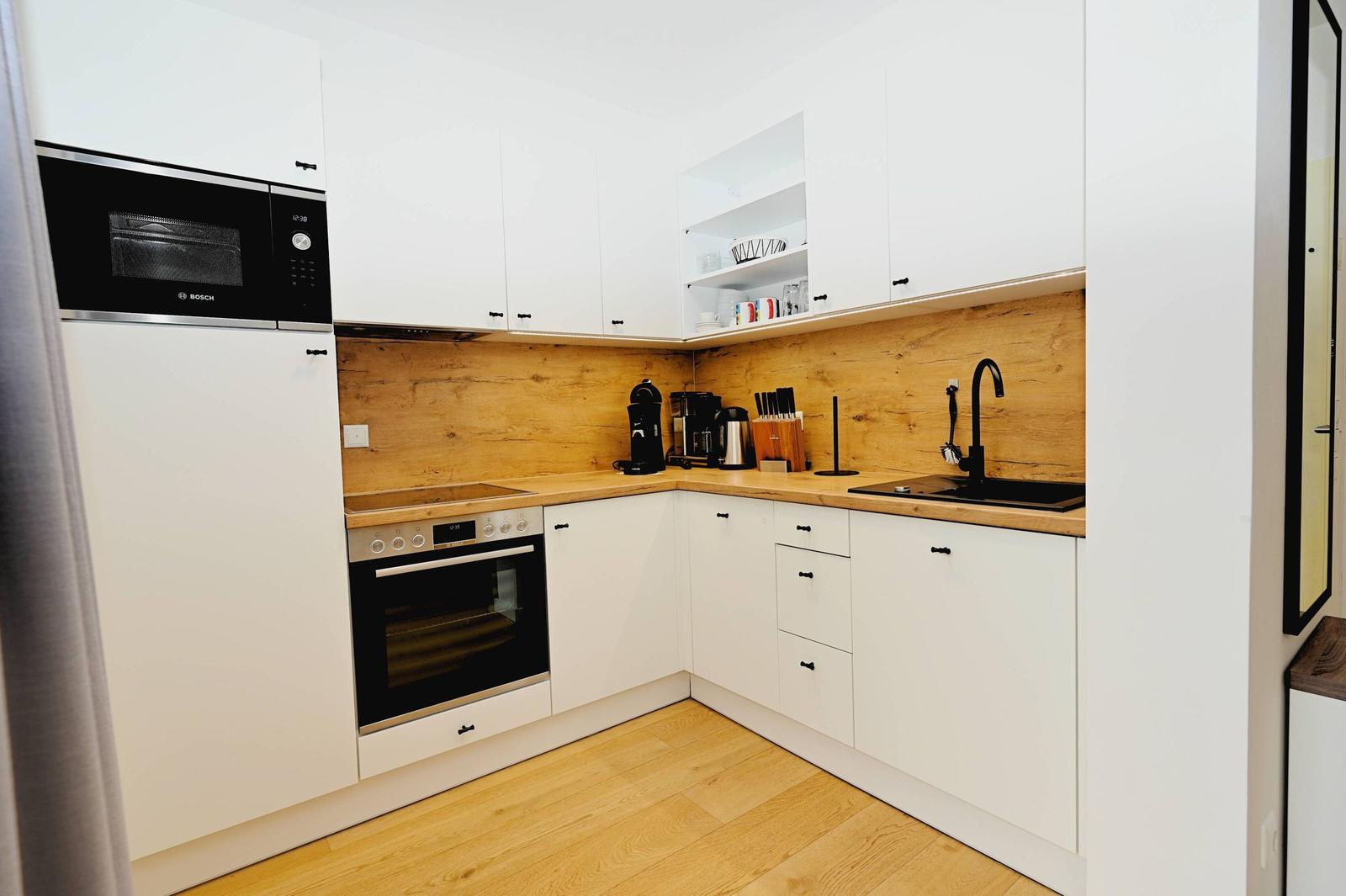 Küche mit weißen Schränken, Holzrückwand und Edelstahlgeräten.