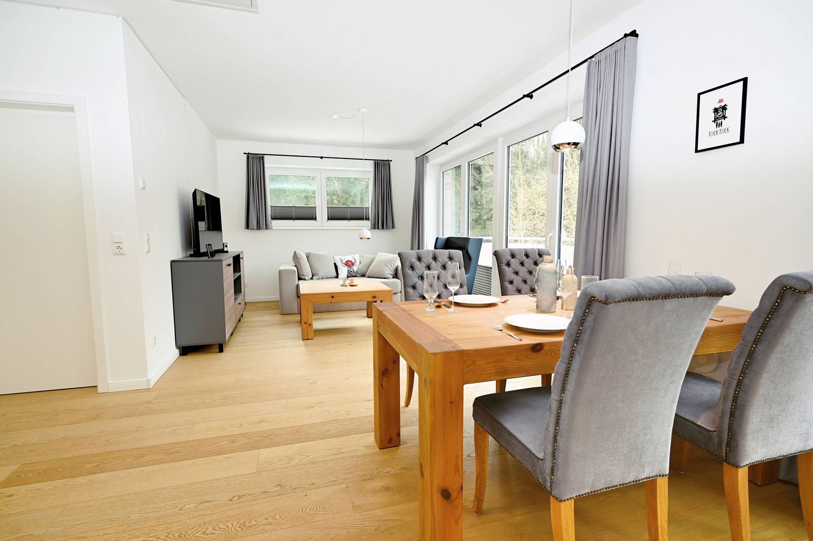 Esszimmer mit Holztisch und Stühlen. Wohnbereich mit Sofa und Fernseher.