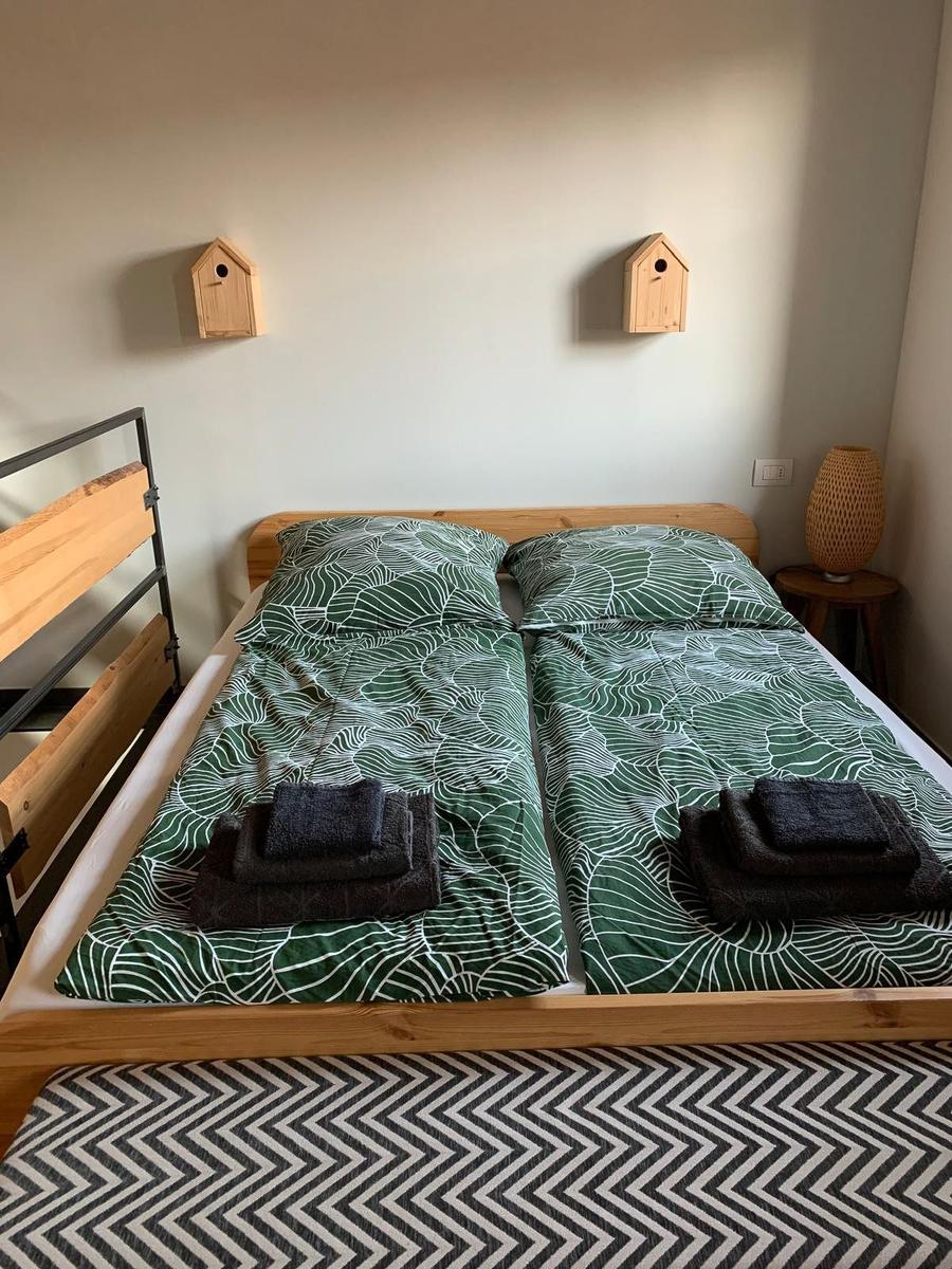Zwei Betten mit grün-weißem Bettzeug und gefalteten Handtüchern. Wanddekoration mit Holzhausfiguren.