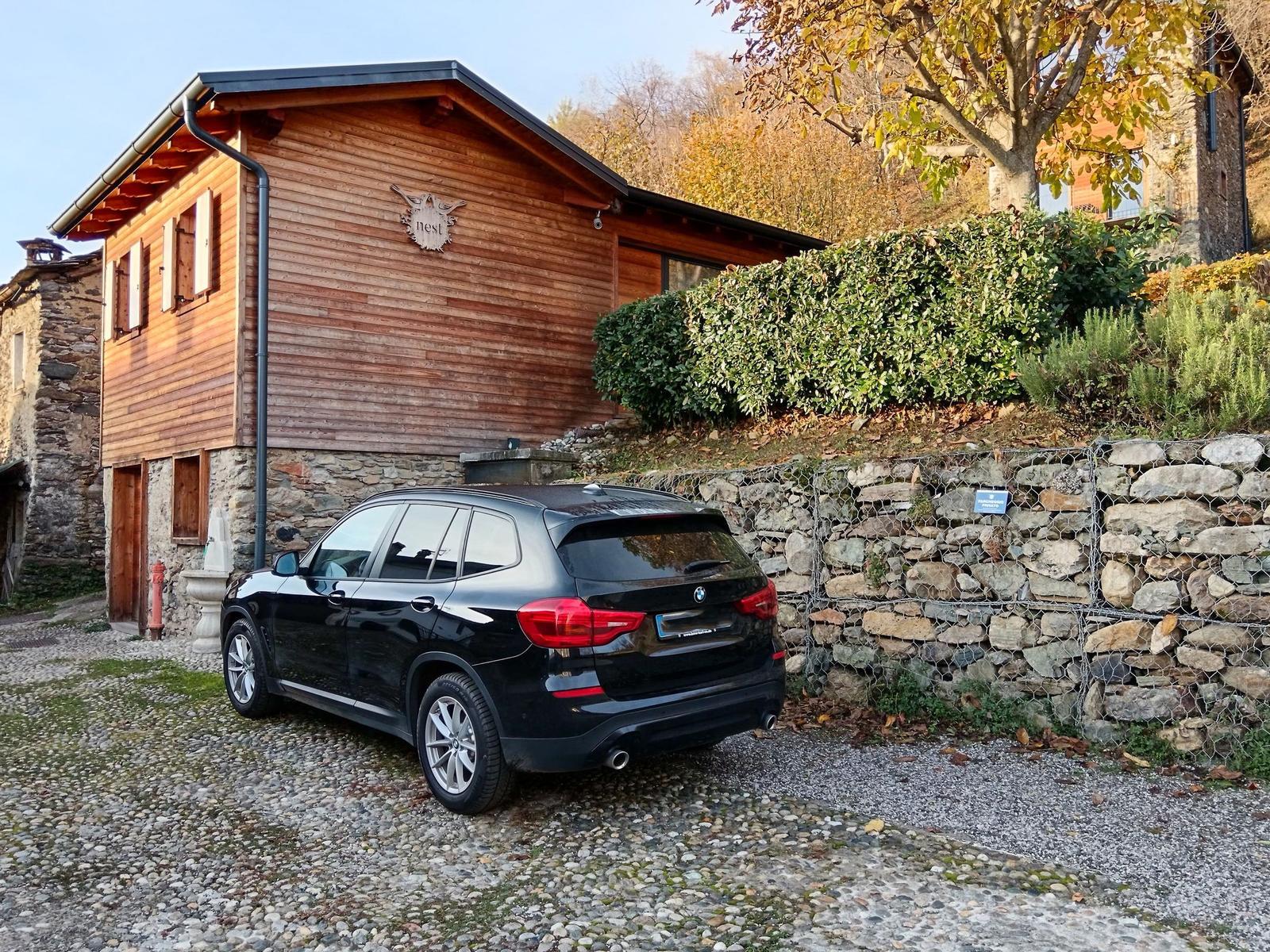 Holzhaus mit Steinmauer und gepflastertem Hof. Ein schwarzes Auto steht vor dem Haus.