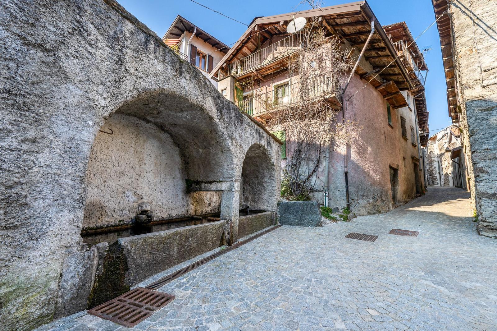 Steinerner Brunnen in einer gepflasterten Gasse mit traditionellen Häusern.