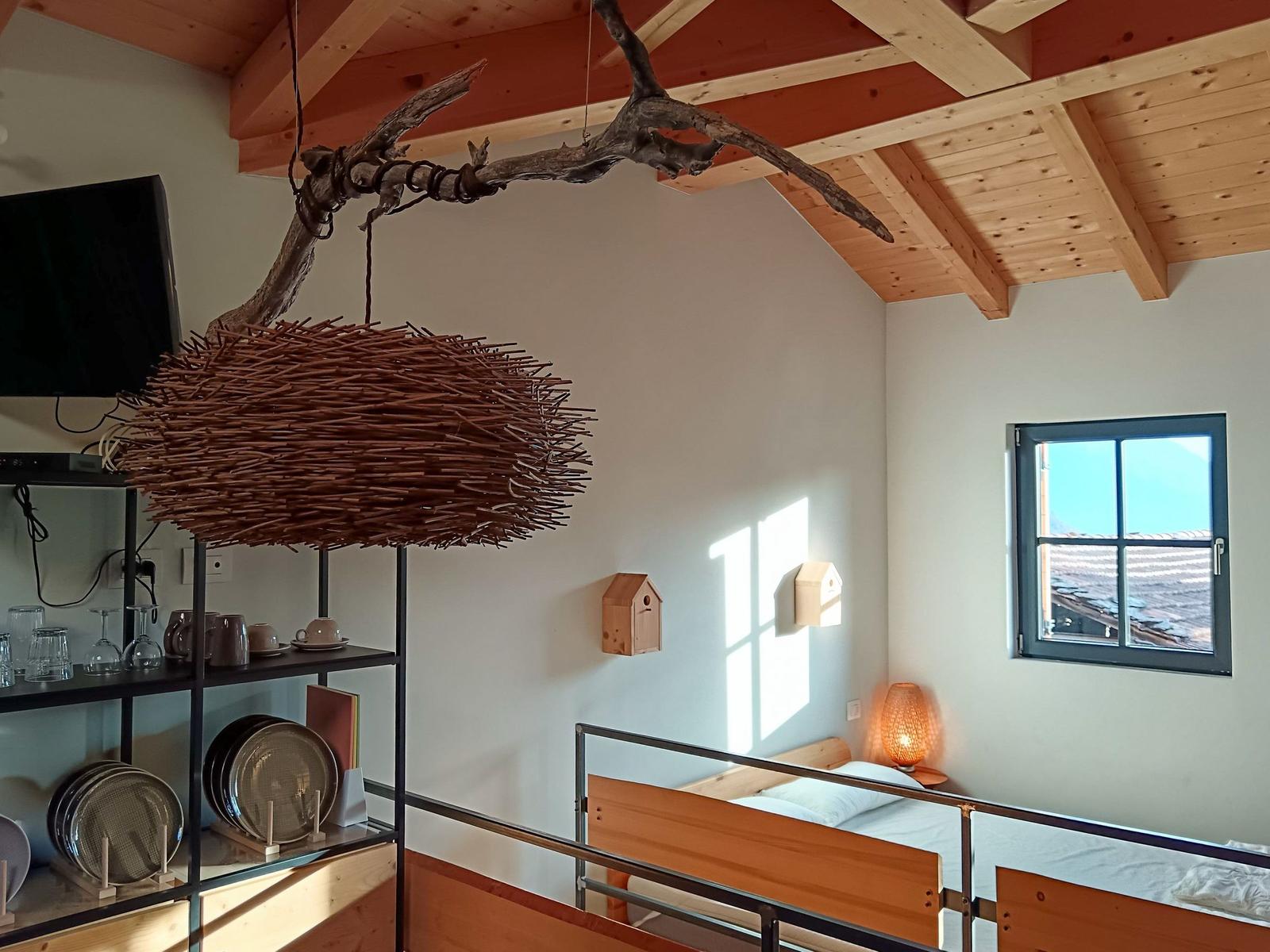 Schlafzimmer mit Holzbett, Fenster und Deckenbalken. Hängende Lampe aus Zweigen.