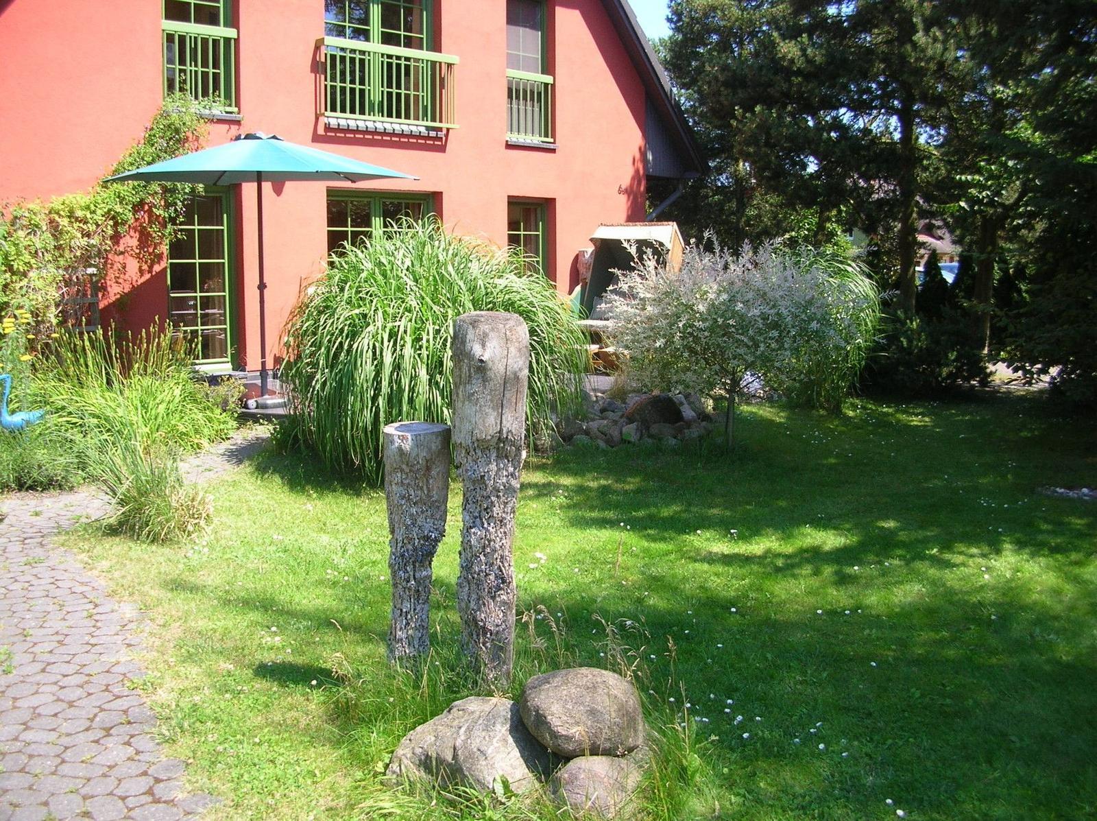 Rotes Haus mit grünen Fenstern, Garten mit Steinen und Sonnenschirm.
