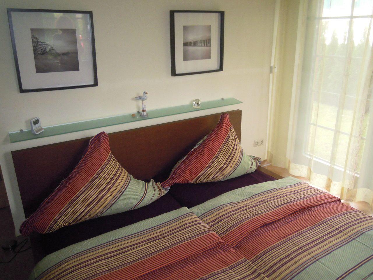 Schlafzimmer mit Bett, Wandbildern und Fenster mit Vorhängen.