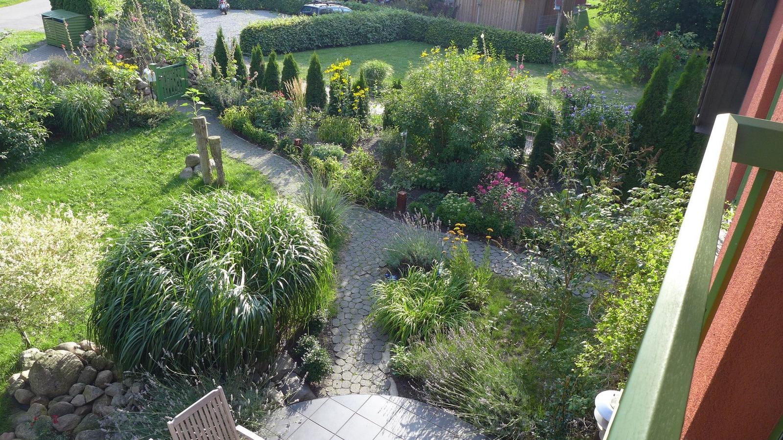 Garten mit Steinsäule, Blumenbeete und gepflastertem Weg von Balkon aus gesehen