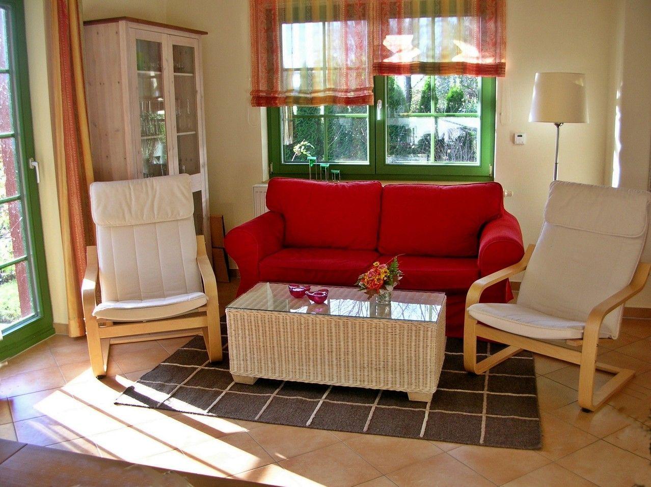 Ein Wohnzimmer mit rosem Sofa, zwei weißen Sesseln und einem Glas-Tisch.