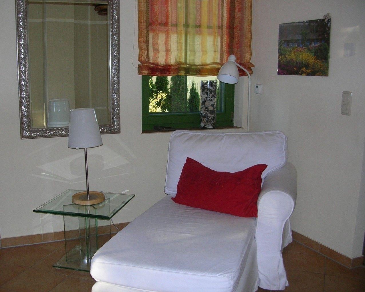Weißes Sofa mit rotem Kissen, Glas-Tisch, Wandspiegel und Fenster mit Vorhang.