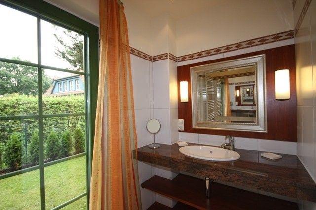 Badezimmer mit Waschtisch, Spiegel und Fenster zur grünen Außenansicht.