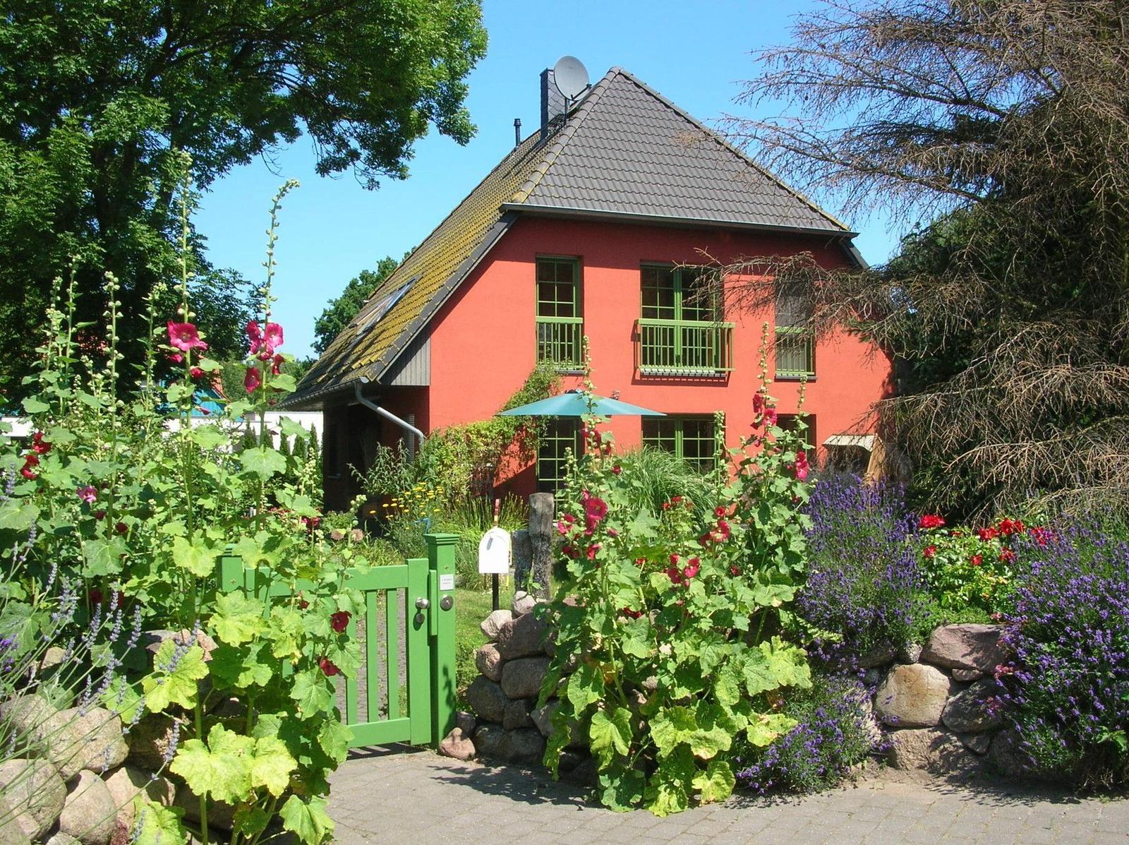 Rotes Haus mit grünem Tor und blühendem Garten.