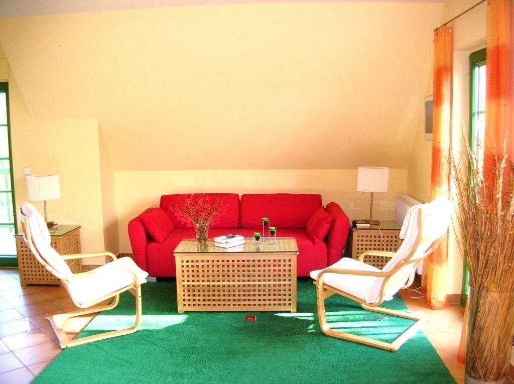 Ein Wohnzimmer mit rotem Sofa, zwei weißen Sesseln und einem Holztisch.