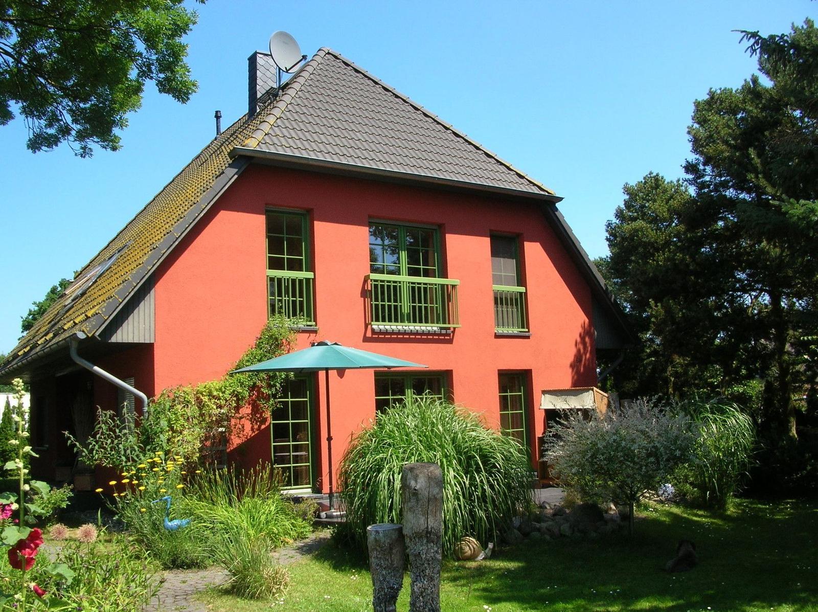 Rotes Haus mit grünen Fenstern und Garten unter blauem Himmel.