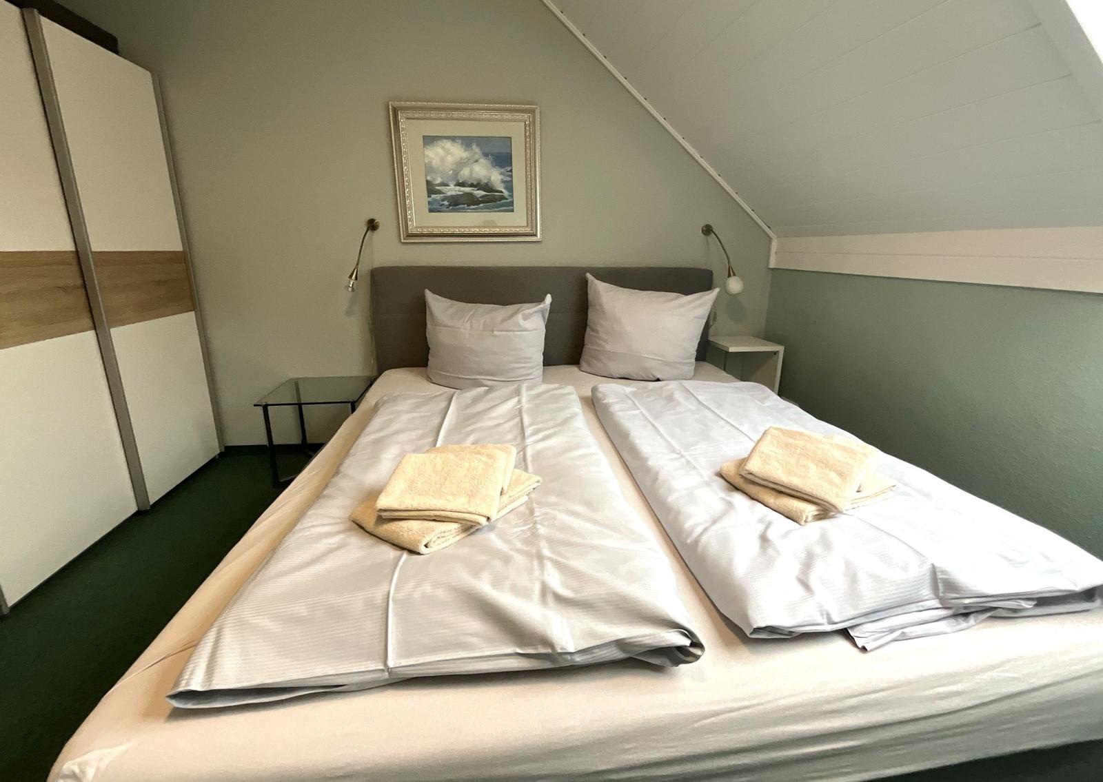 Schlafzimmer mit Doppelbett, Nachttischen und Wandbild unter Dachschrägen.