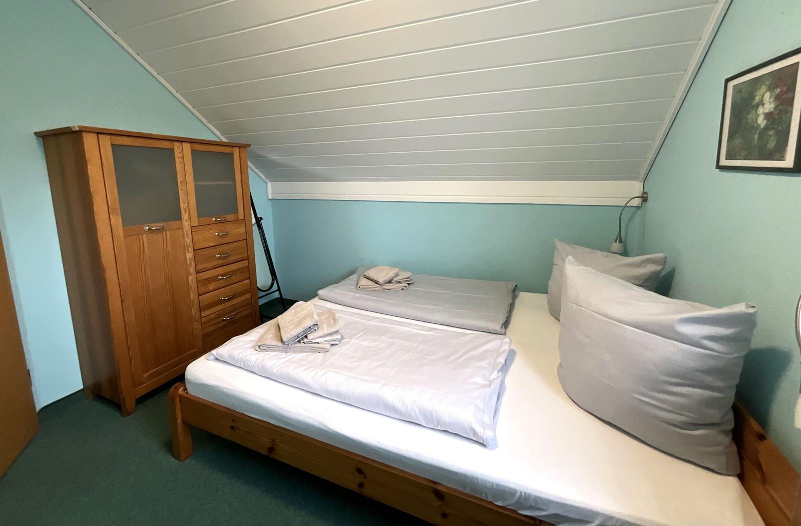 Zimmer mit Doppelbett, Holzschrank und gemalten Wänden.