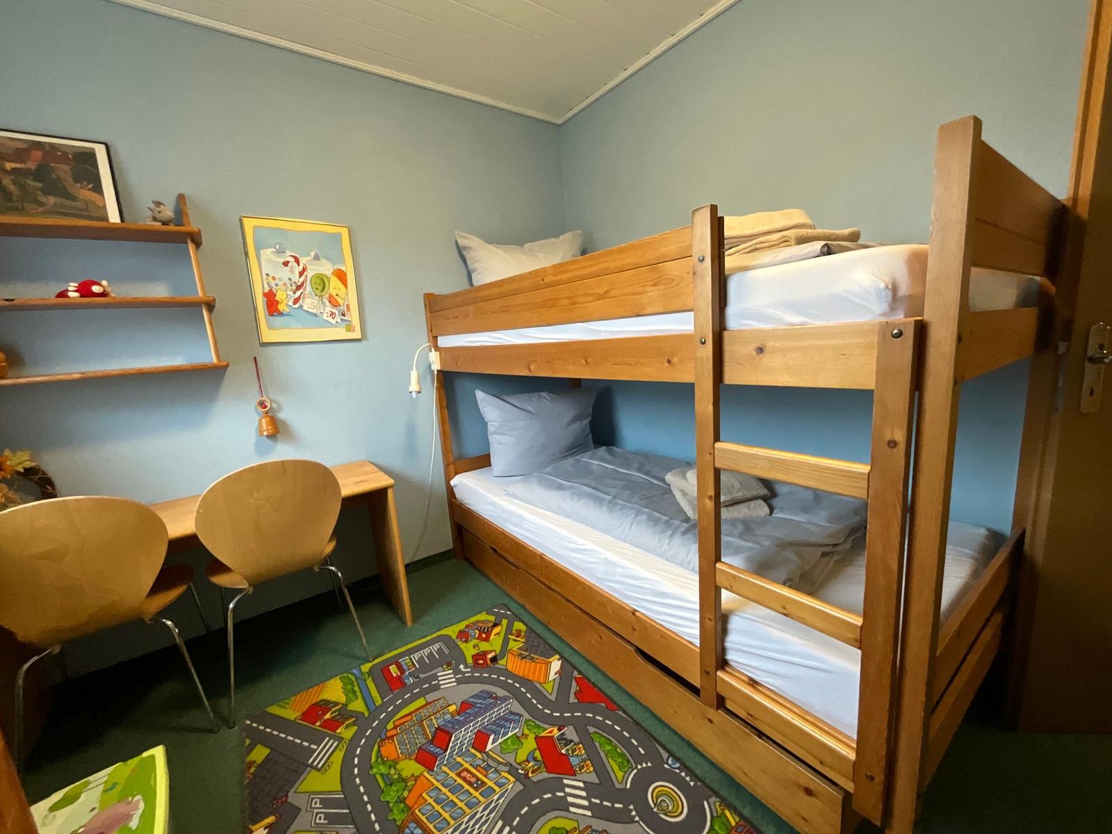 Ein Zimmer mit einem Holz-Etagenbett, einem Schreibtisch und einem Spielteppich.