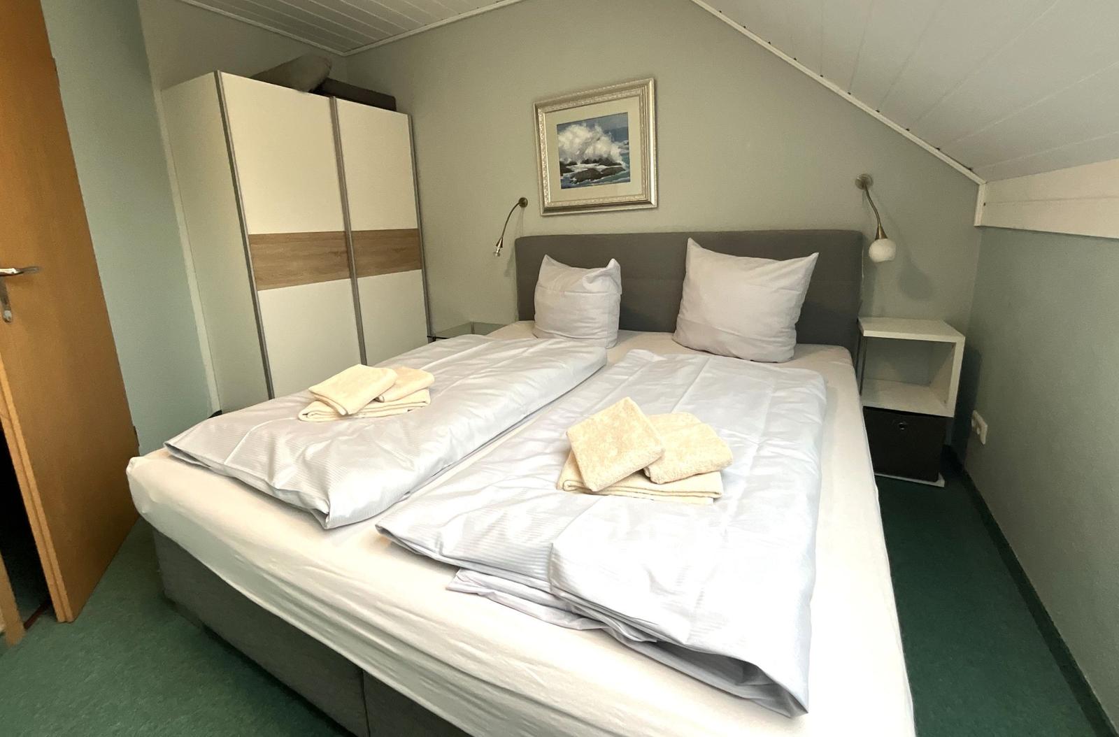 Schlafzimmer mit Doppelbett, Kleiderschrank und Nachttischen unter Dachschrägen.