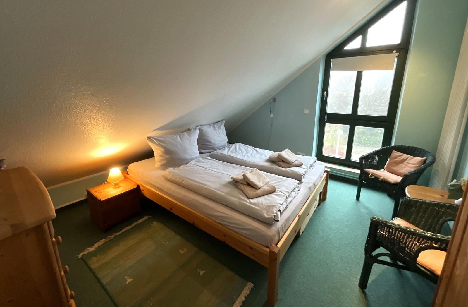 Zimmer mit Doppelbett, Sitzgelegenheit und großem Fenster