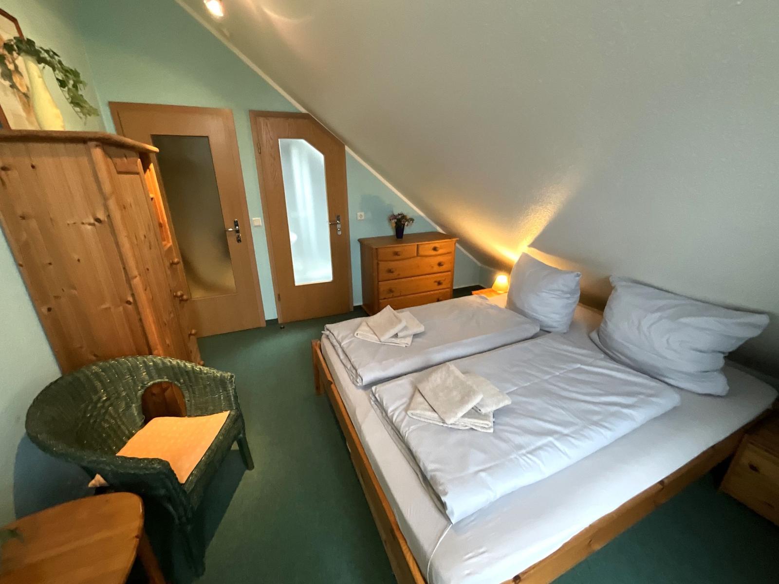 Schlafzimmer mit Doppelbett, Holzmöbel und schräger Decke.